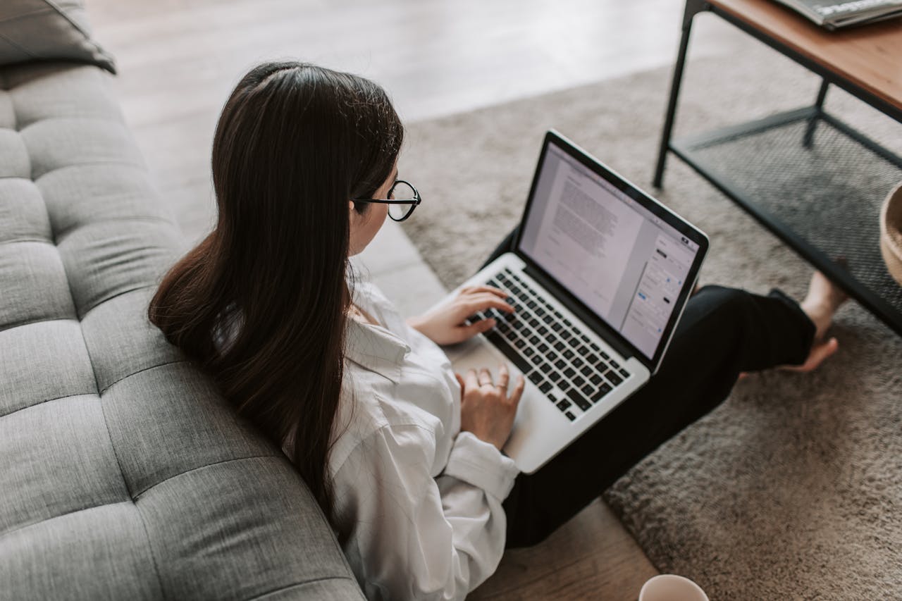 service-02 Woman working remotely with a laptop on the floor next to a sofa, enjoying comfortable home office setup.