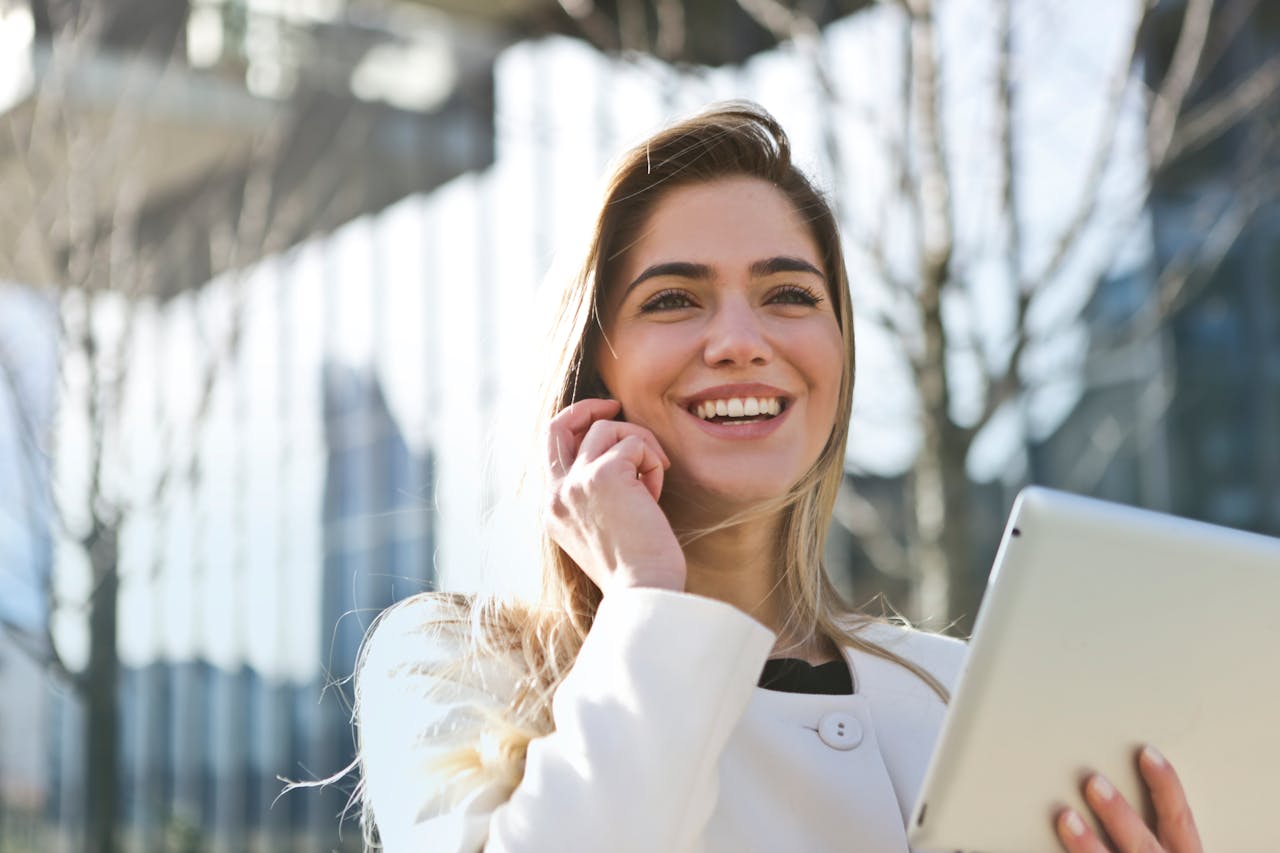 service-03 Confident businesswoman using her tablet and phone, smiling outdoors in sunlight.